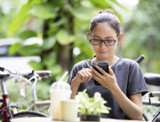 Young Asian woman  using smartphone in garden, looking on screen.