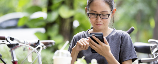 Young Asian woman  using smartphone in garden, looking on screen.